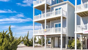 Edificio frente a la playa con varios pisos, balcones, una señalización de dirección visible y cielo despejado.