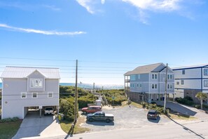 Rua residencial com casas, céu claro e vista distante do oceano.