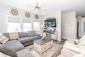 Sala de estar com sofá seccional, mesa de centro, televisão e decoração com tema náutico.