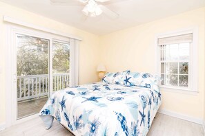 Un dormitorio con cama, ventilador de techo y ventana con vista a árboles.
