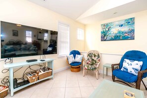 A living room with a television, wicker chairs, a small table, and a painting on the wall.