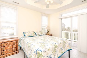 A bedroom with a bed, a nightstand, a dresser, and a view of the outside.