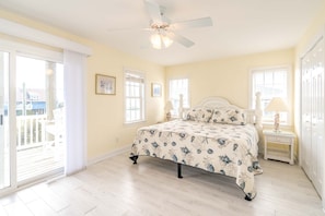 A bedroom with a bed, a ceiling fan, a window, and a door.