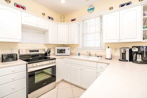 A modern kitchen with white cabinets, a stainless steel stove, a microwave, and a coffee maker.