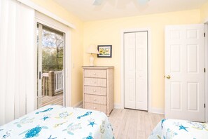 A bedroom with two beds, a chest of drawers, a door, and a window.