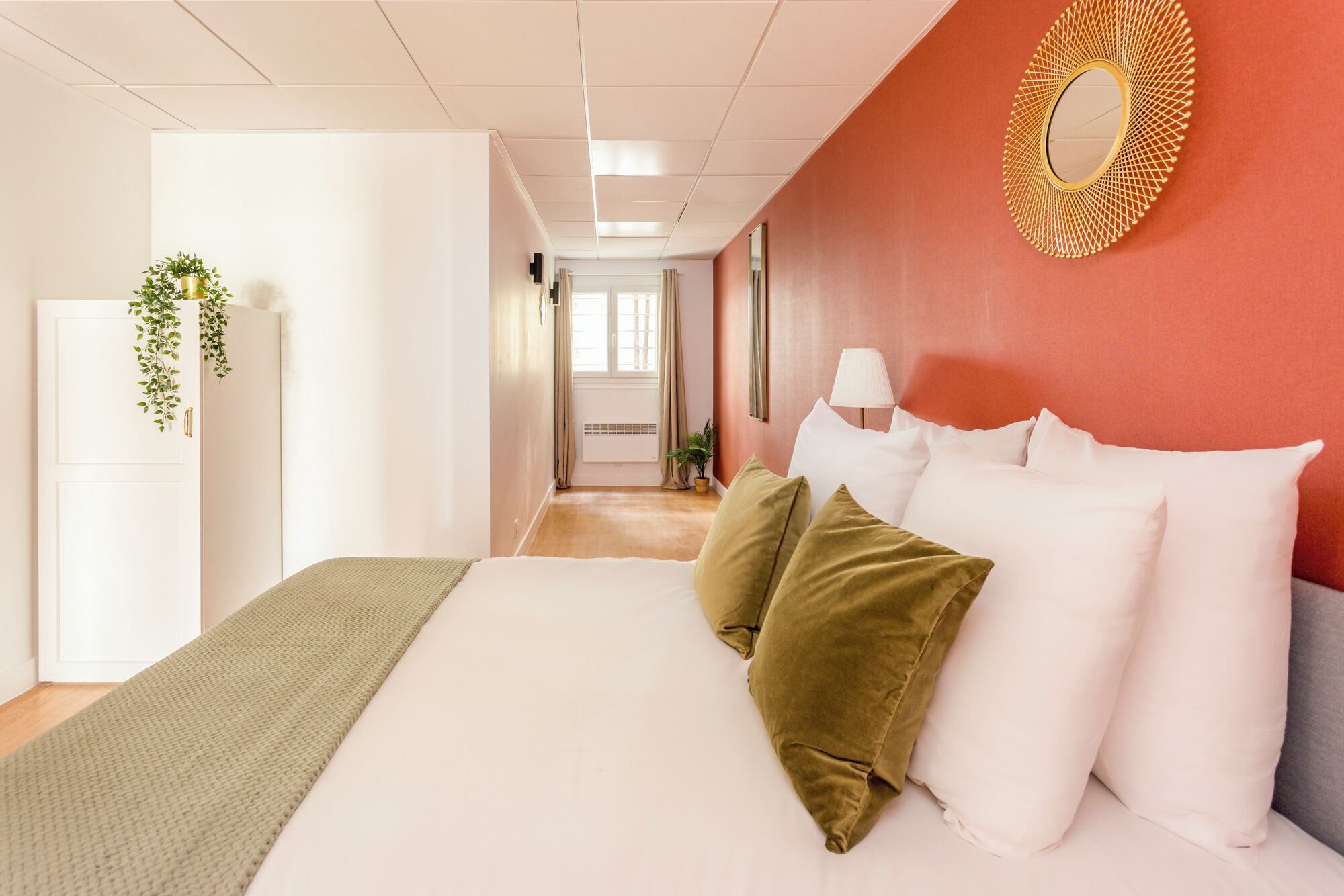 Una camera d'hotel con un letto, uno specchio, una lampada e vista su un corridoio.