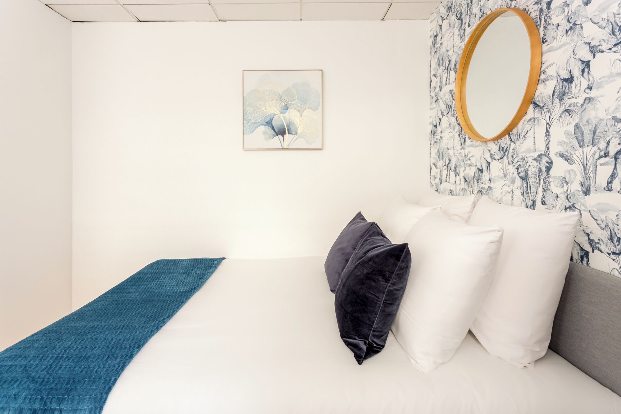 Ein Schlafzimmer mit einem Bett, einer blauen Tagesdecke, einem gerahmten Bild und einem Spiegel an der Wand.