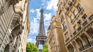 A view of the Eiffel Tower between two buildings with classical architecture, featuring ornate balconies and detailed stonework. - Family Suite - Marais - Pelee (Paris)