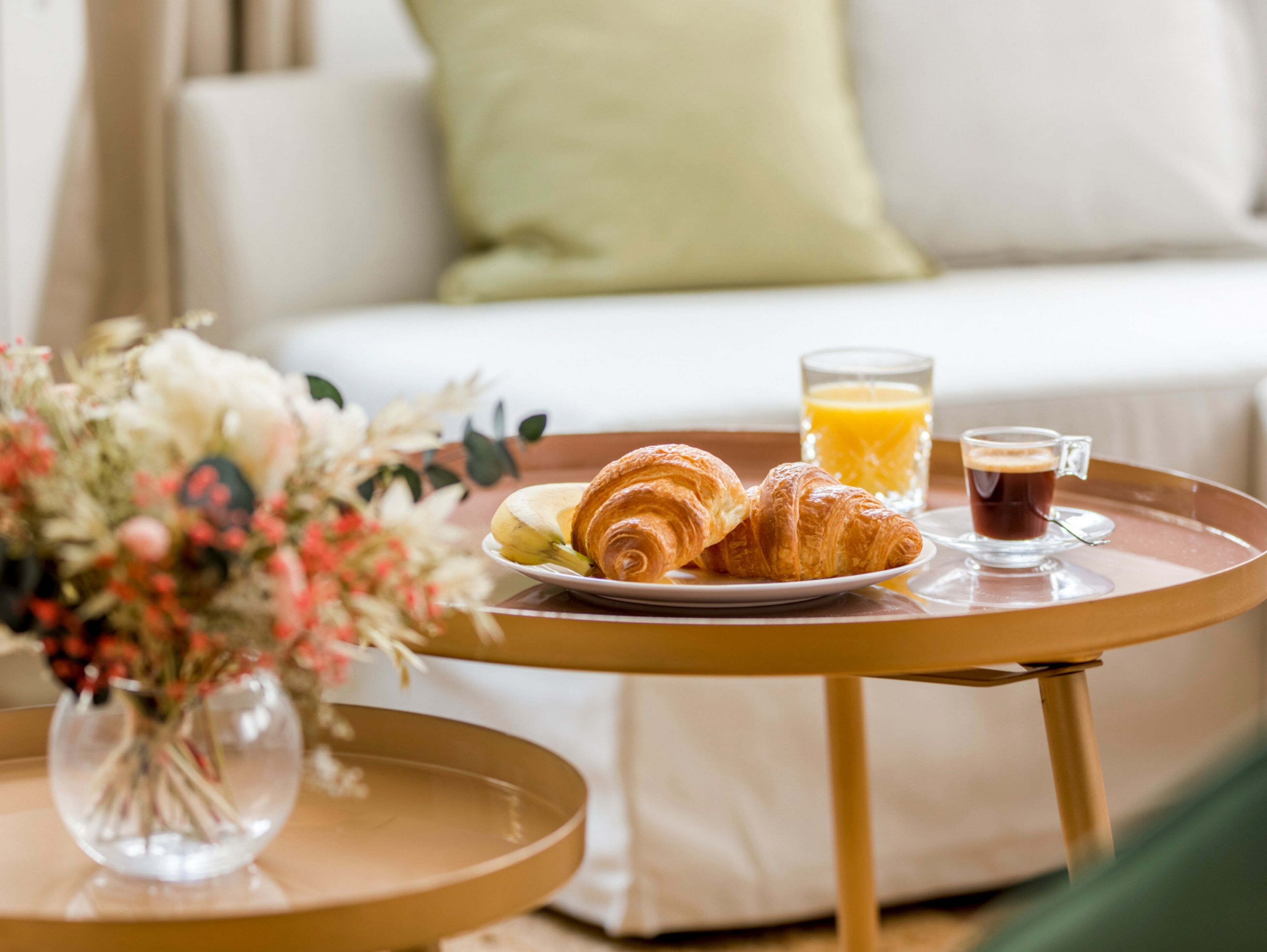 A breakfast tray with croissants, a glass of orange juice, and a cup of coffee on a round table.