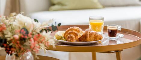 A breakfast tray with croissants, a glass of orange juice, and a cup of coffee on a round table.