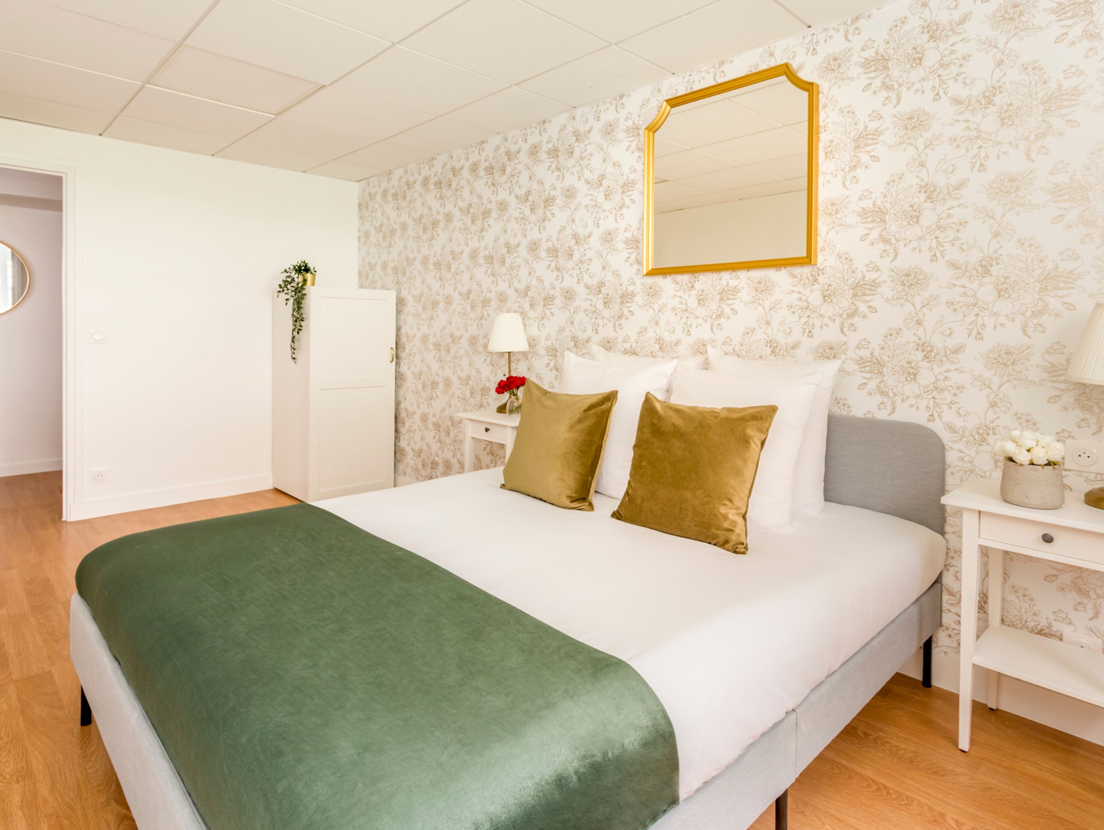 A neatly arranged bedroom with a bed, a nightstand, a mirror, and a door.