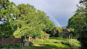 Ländliche Landschaft mit einem Haus, üppigem Grün und einem Regenbogen.