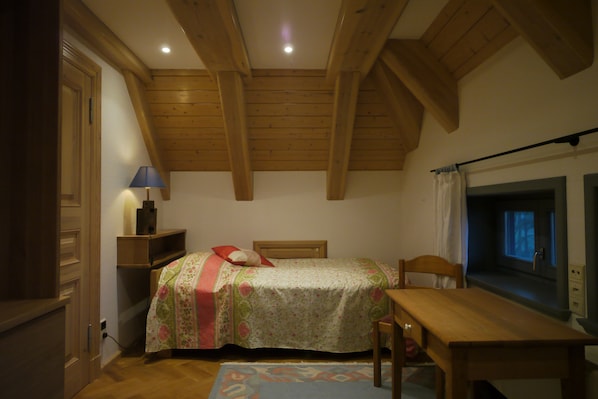 A bedroom with a bed, a table, a lamp, and a window with curtains.