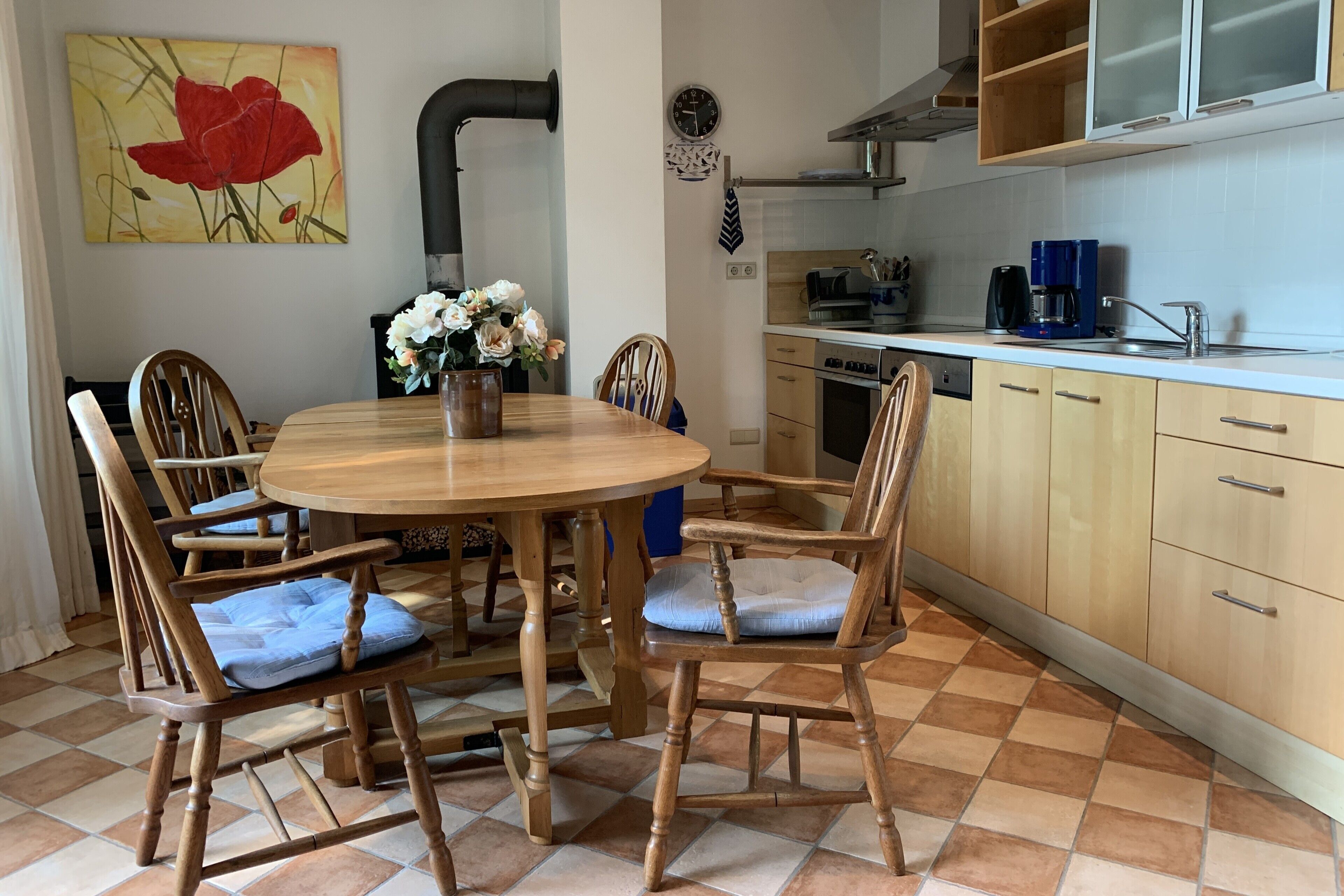 Un'area pranzo con un tavolo rotondo in legno, sei sedie e un vaso di fiori.