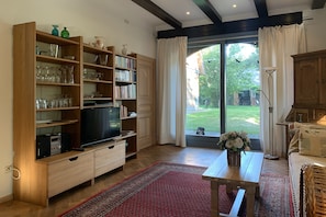 Ein Wohnzimmer mit Fernseher, Bücherregalen, einem Couchtisch und Blick ins Freie.