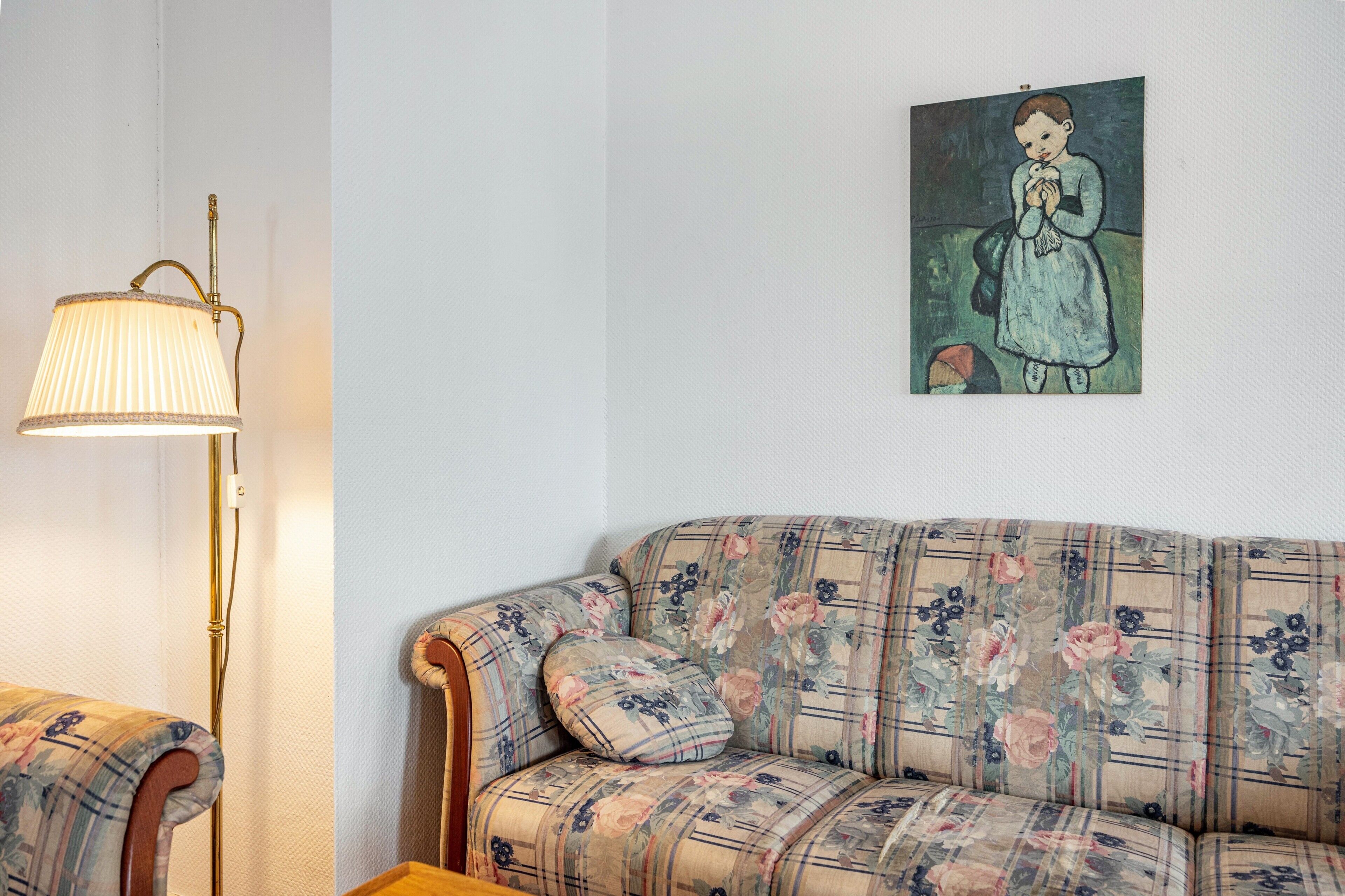 Een kamer met een bank, een lamp en een schilderij aan de muur.