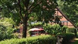 Un jardín con una sombrilla roja, un edificio de ladrillo y una estructura de madera.