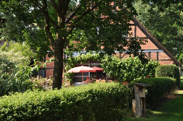 Ein Garten mit einem roten Sonnenschirm, einem Backsteinhaus und einer Holzkonstruktion.