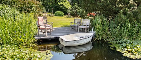 Eine ruhige Außenterrasse mit einem angestauten Boot, umgeben von üppiger Vegetation und einem friedlichen Teich mit Seerosen.