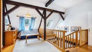 Une chambre avec un plafond en bois, un lit, un bureau, une chaise, une fenêtre avec des rideaux et un escalier.