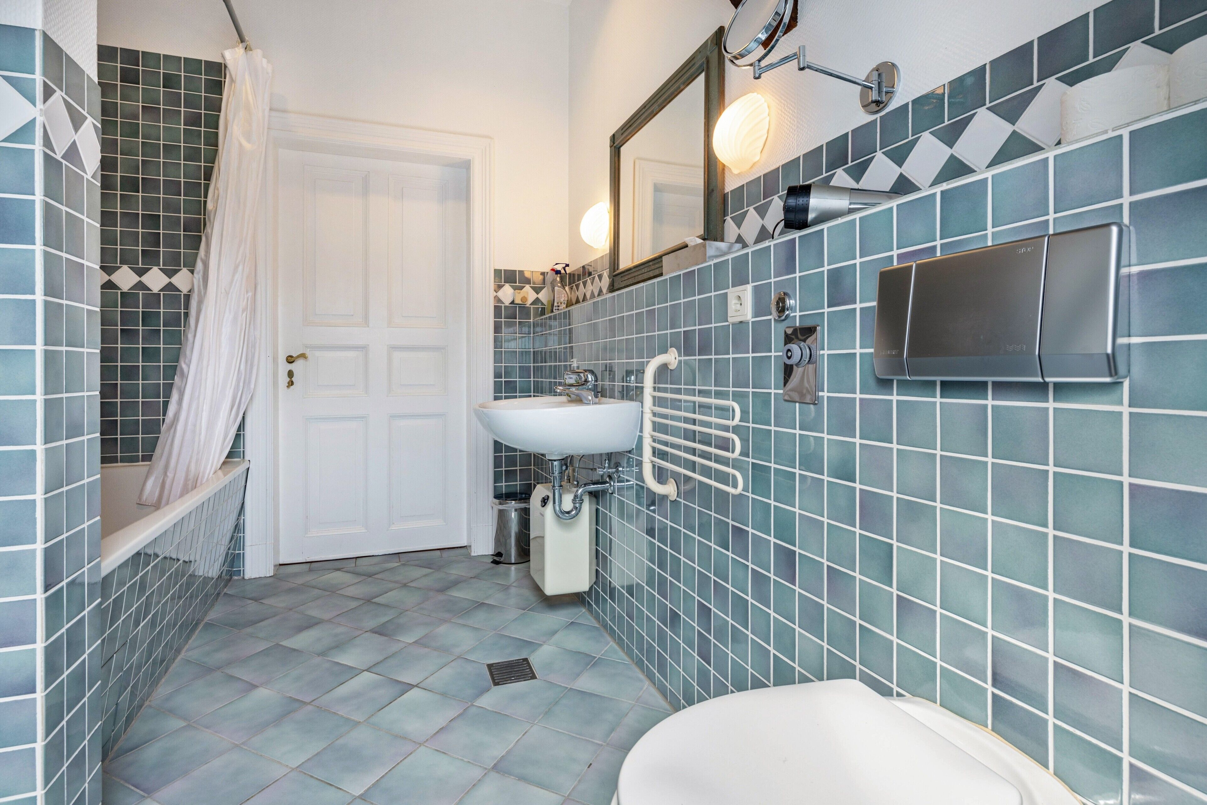 Ein Badezimmer mit einer weißen Tür, einer Duschkabine mit Vorhang, einem Waschbecken mit Handtuchhalter und einem Spiegel über dem Waschbecken.