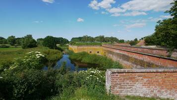A historic brick structure with a river in the foreground, surrounded by greenery and trees.
