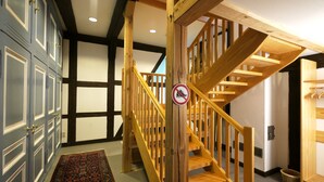 Una escalera con barandilla de madera y un cartel que prohíbe zapatillas, que conduce a una habitación con alfombra estampada y una puerta con picaporte decorativo.