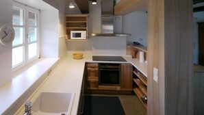Una cocina moderna con microondas integrado, horno y lavaplatos. Hay un bol de madera en la encimera y un reloj en la pared.