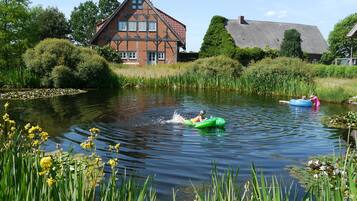 A calm river with two people on inflatable rafts, surrounded by lush greenery and a traditional house.