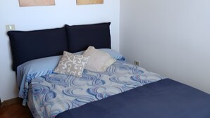 Un lit avec une couvre-lit à motifs bleus et blancs, deux oreillers et une tête de lit sombre.