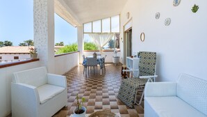 A balcony with white wicker furniture, a checkered floor, and a view of greenery.