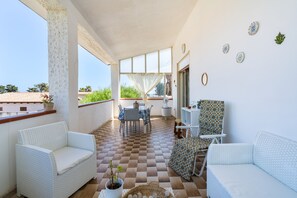 A balcony with white wicker furniture, a checkered floor, and a view of greenery.