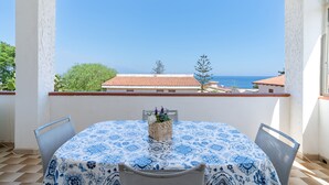 A balcony with a table and chairs, overlooking a coastal view with buildings and trees.