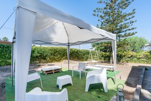 A covered outdoor seating area with white plastic furniture and a white canopy.