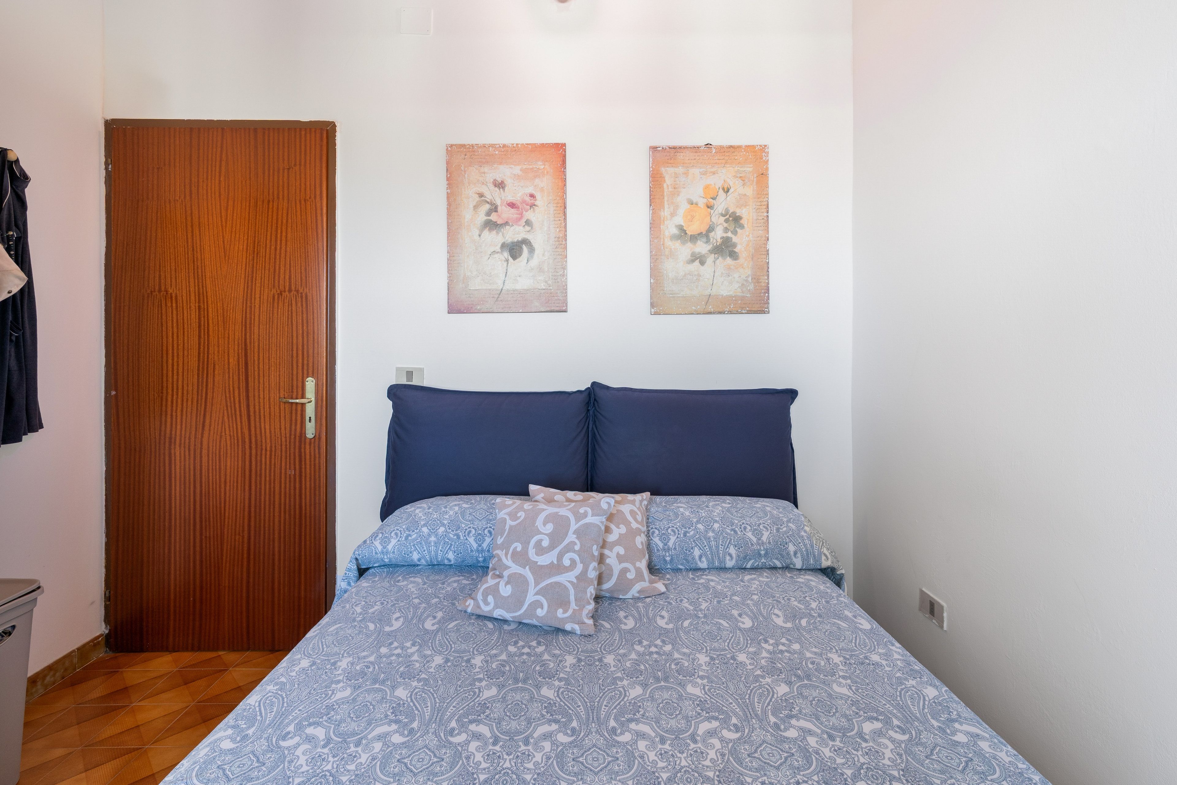 Ein Schlafzimmer mit einer Holztür, einem Bett mit gemusterten Betttextilien und zwei an der Wand befestigten Bildern.