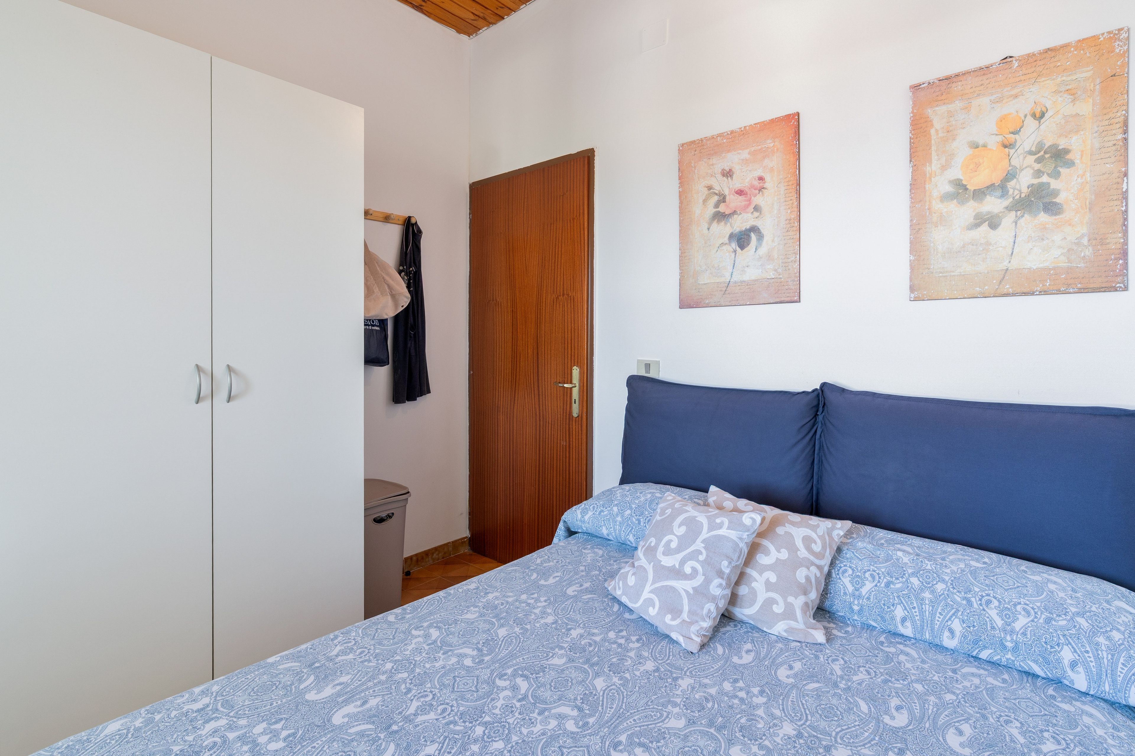 A bedroom with a bed, a wardrobe, a door, and two wall-mounted paintings.