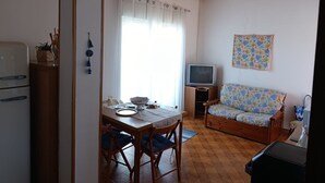 Un espace de vie compact comprenant un coin repas, un canapé, un téléviseur et une kitchenette.