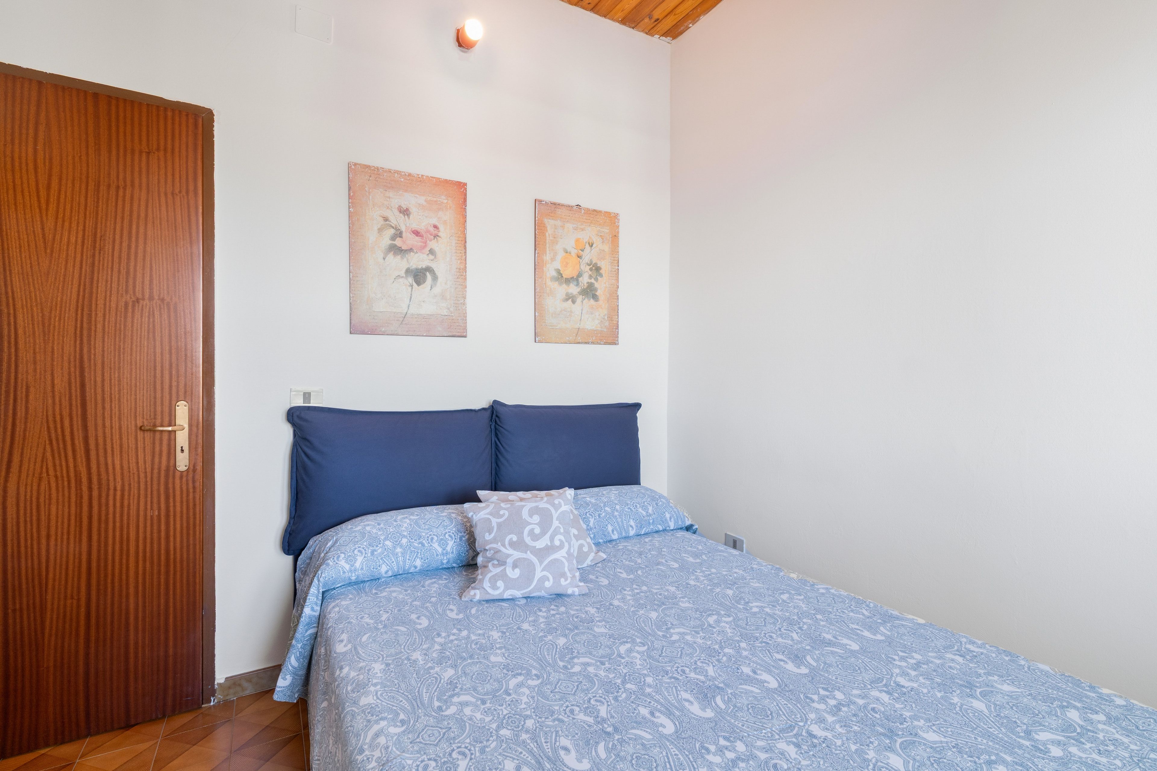 Un dormitorio con puerta de madera, una cama con ropa de cama azul y dos cuadros colgados en la pared.
