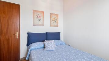 Un dormitorio con puerta de madera, una cama con ropa de cama azul y dos cuadros colgados en la pared.