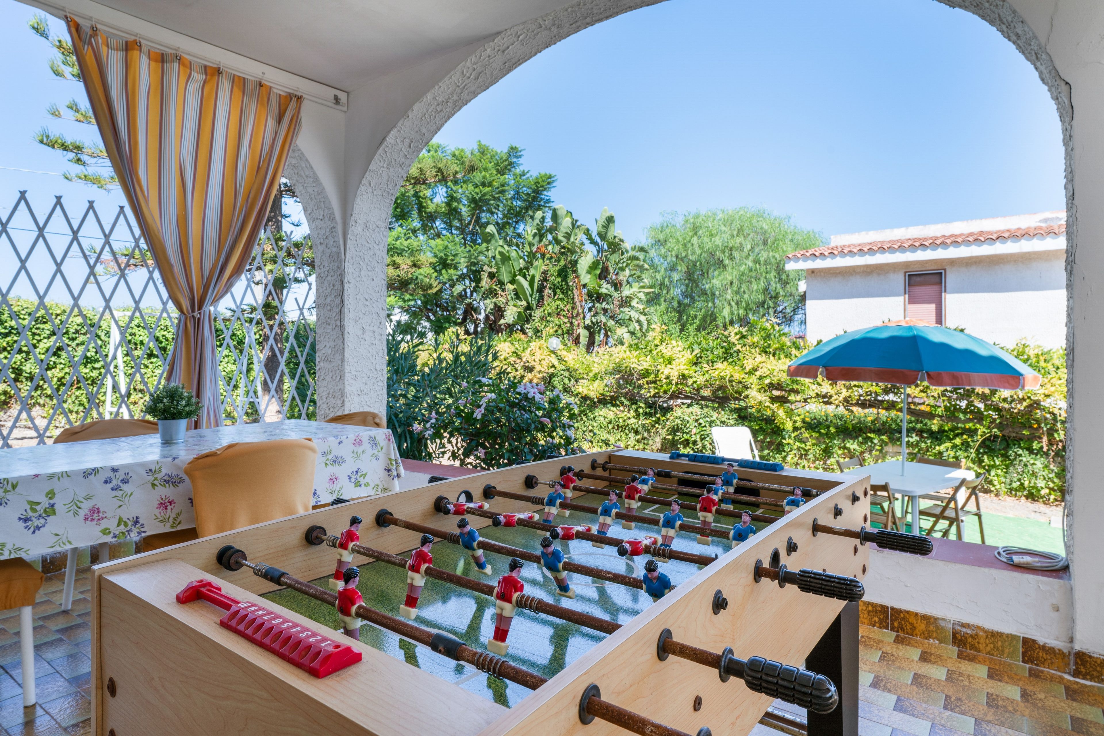 A foosball table in an outdoor patio area with a view of a house and greenery.