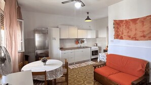 A compact living space with a dining area, kitchenette, and a sofa. - Casa Orchidea with Veranda – Private Terrace, Wi-Fi & Air Conditioning (Costa Saracena - Castelluccio)