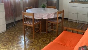 A compact kitchen with a refrigerator, a dining table with chairs, and a sofa. - Casa Orchidea with Veranda – Private Terrace, Wi-Fi & Air Conditioning (Costa Saracena - Castelluccio)
