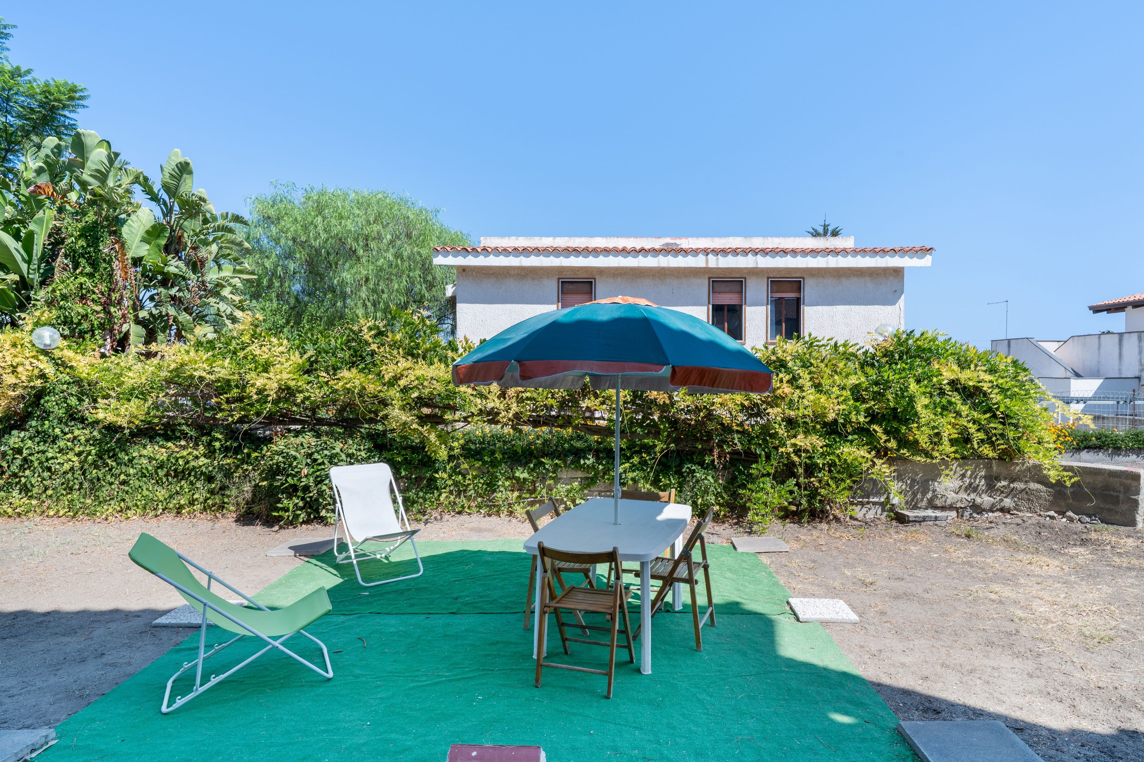 Eine Terrasse mit Tisch und Stühlen, eine grüne Rasenfläche und ein Gebäude im Hintergrund.