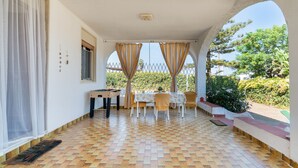 A covered patio with a foosball table, a dining table with chairs, and a view of greenery. - Casa Orchidea with Veranda – Private Terrace, Wi-Fi & Air Conditioning (Costa Saracena - Castelluccio)
