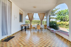 A covered patio with a foosball table, a dining table with chairs, and a view of greenery. - Casa Orchidea with Veranda – Private Terrace, Wi-Fi & Air Conditioning (Costa Saracena - Castelluccio)