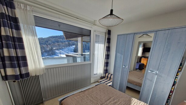 A bedroom with a bed, a window with curtains, a radiator, a wardrobe, and a hanging light fixture. - Apartment for 4 near slopes and activities (Besse-et-Saint-Anastaise-Super Besse)