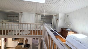 Une chambre avec un lit en mezzanine, une petite table, un ventilateur et une fenêtre donnant sur un balcon.