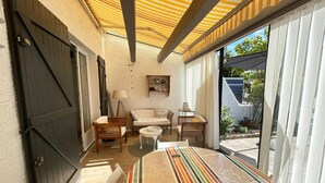 Une terrasse ensoleillée avec une table à rayures, des chaises en bois, un canapé et une lampe.