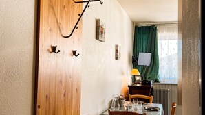 Un comedor con puerta de madera, ganchos, una mesa con vasos, una lámpara y vistas a una ventana con cortinas.