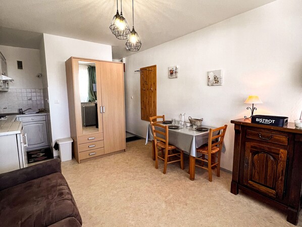 A compact kitchen with a dining area, a wooden wardrobe, and a small table set for two.